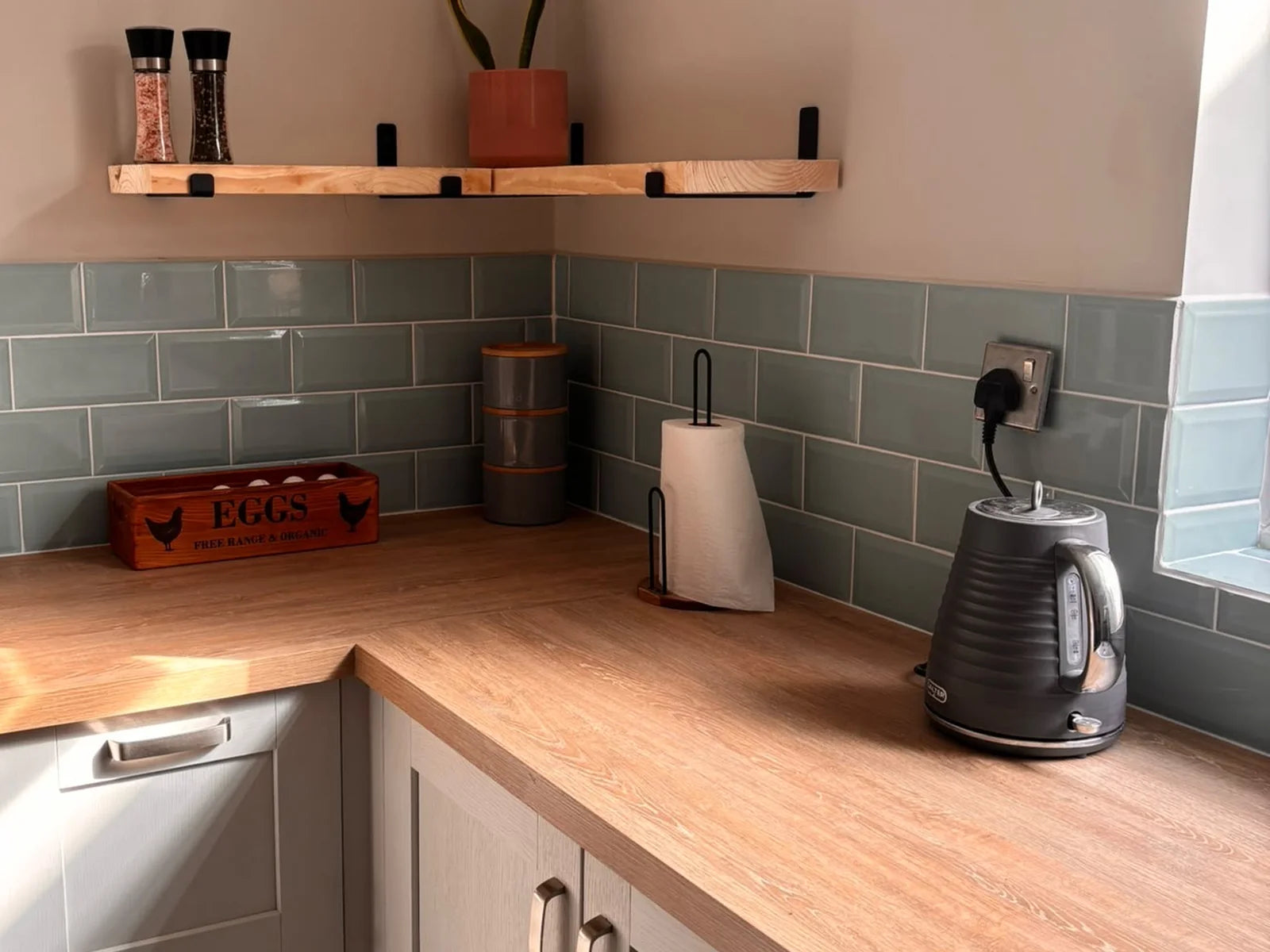 Finished kitchen with light cabinetry, oak-effect worktops and blue metro tiles